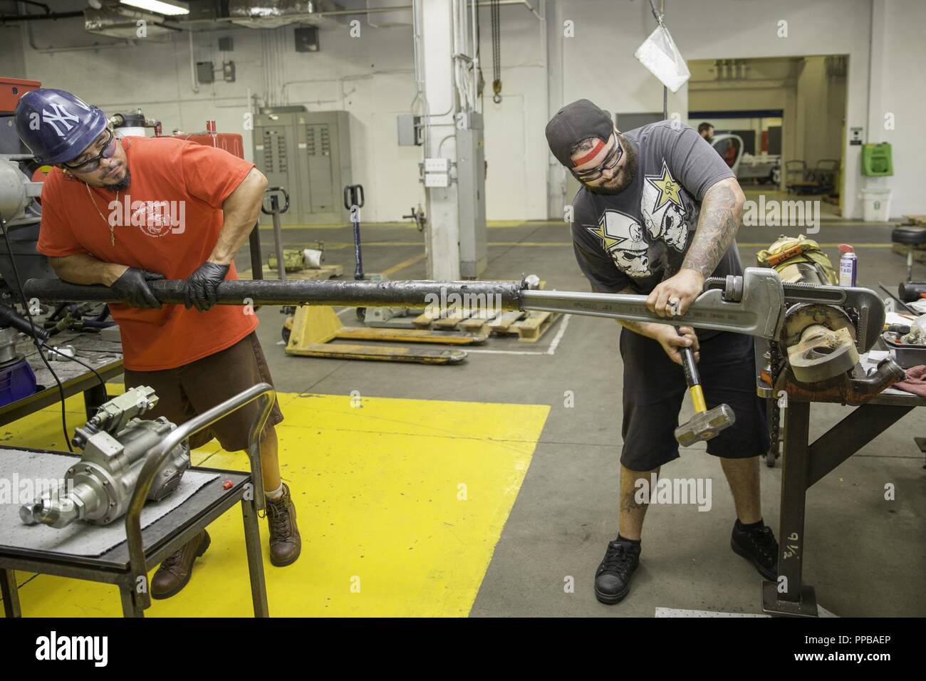 department-of-defense-civilian-employees-cory-moya-and-jose-rivera-heavy-equipment-mechanics-use-a-large-pipe-wrench-and-cheater-bar-to-disassemble-this-hydraulic-cylinder-at-the-production-plant-aboard-marine-corps-logistics-base-barstow-california-aug-17-the-hydraulic-resevoir-is-pressurized-and-used-to-move-large-objects-such-as-hatches-up-and-down-PPBAEP.jpg